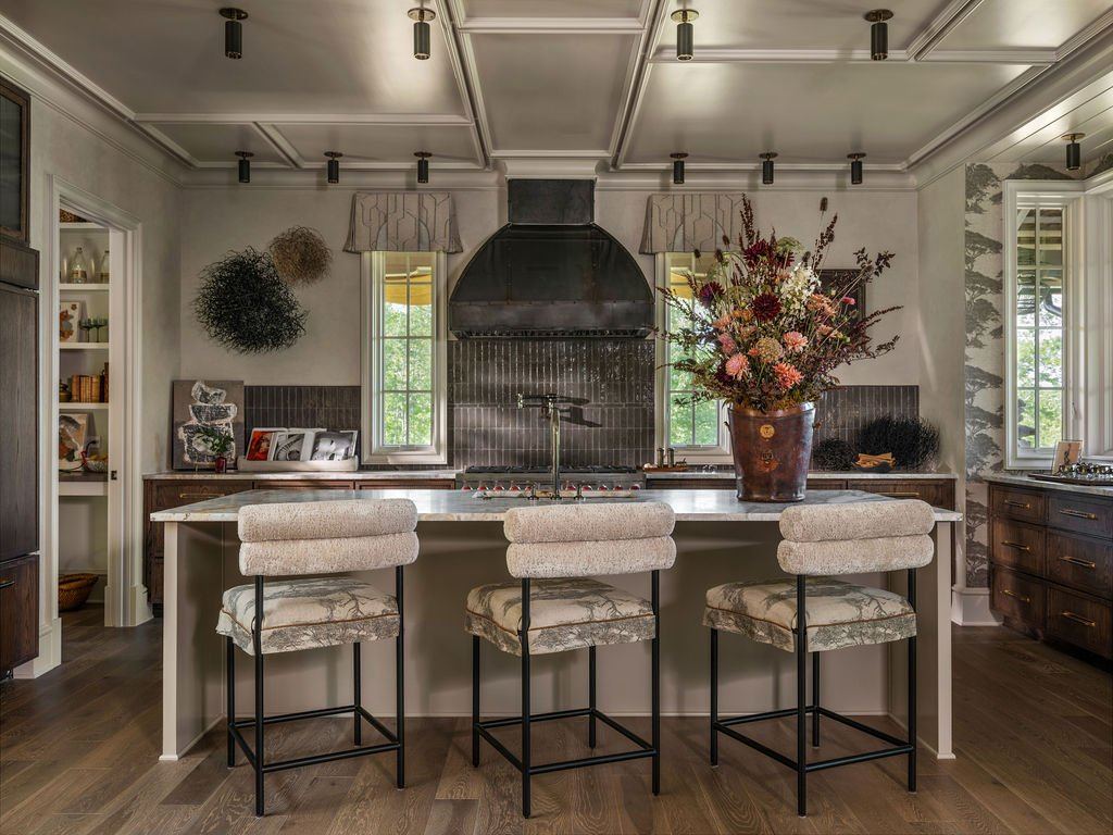 Kitchen with a black range hood, upholstered counter stools, and a dried floral arrangement