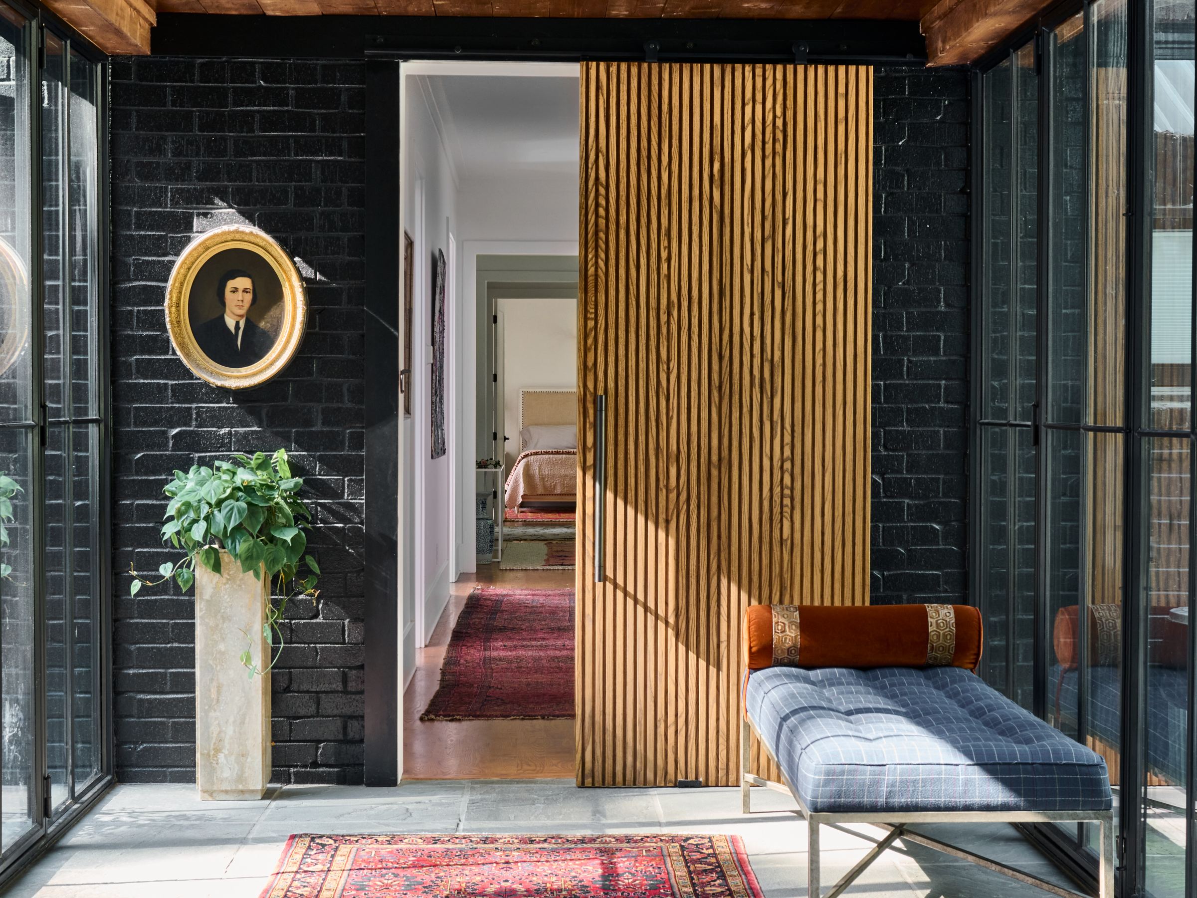 Entry with black-painted brick, a fluted wood door, a vintage portrait, and an upholstered bench