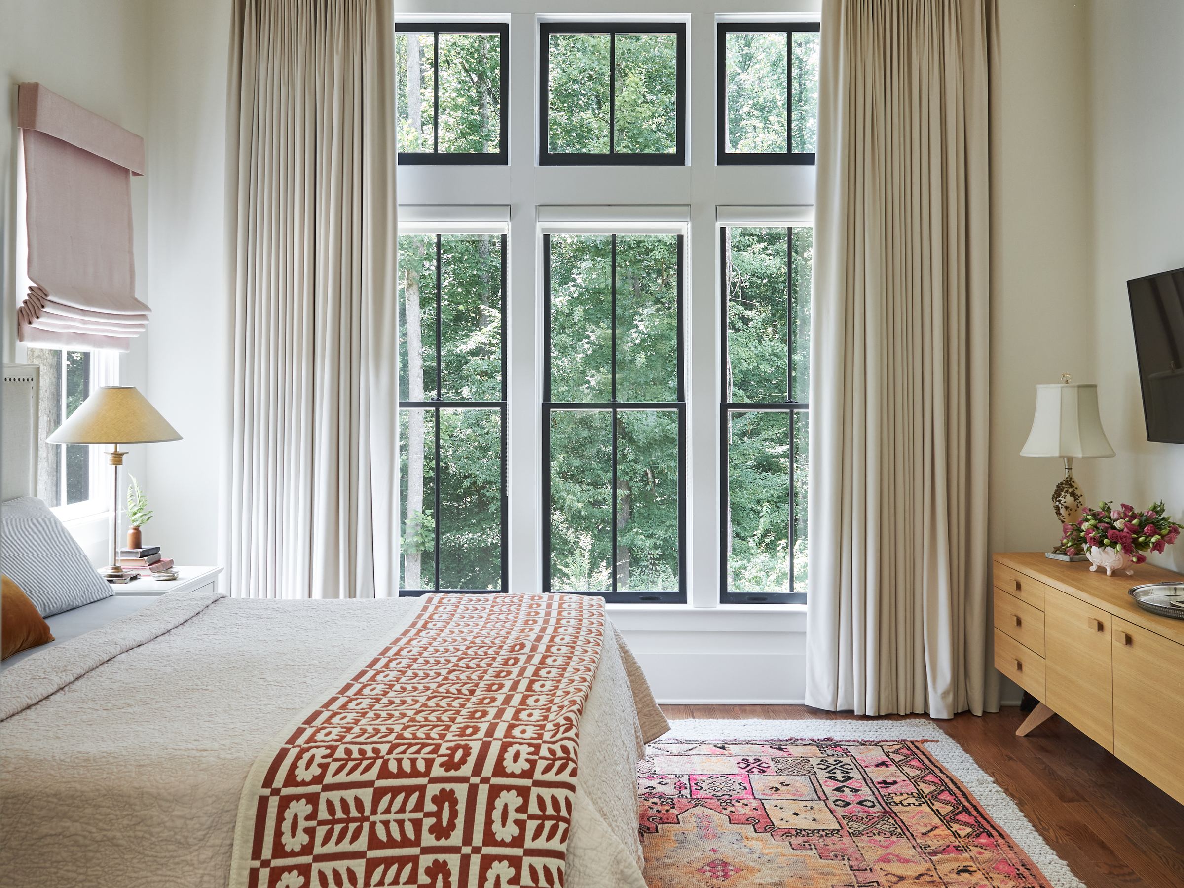Bedroom with tall black-framed windows, linen drapery, and a vintage rug